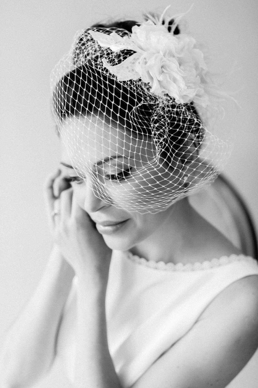 Washington DC photographer black and white bridal portrait: a bride in a birdcage veil smiling as she adjusts her earring.