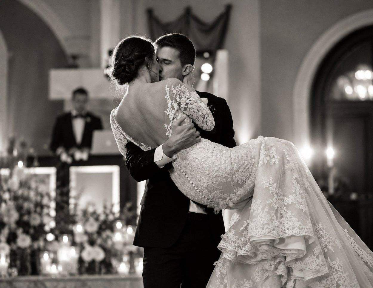 Washington DC photographer black and white wedding photo: a groom carrying his bride in a lace gown and kissing her during their first dance in a candlelit ballroom.