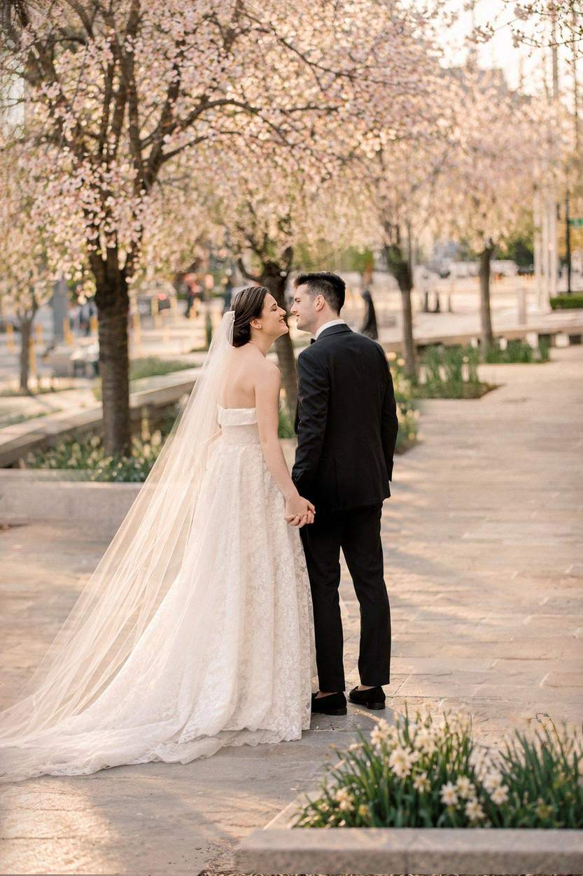 Washington DC photographer wedding portrait: a bride in a long veil and a groom holding hands and smiling at each other beneath blooming cherry trees.